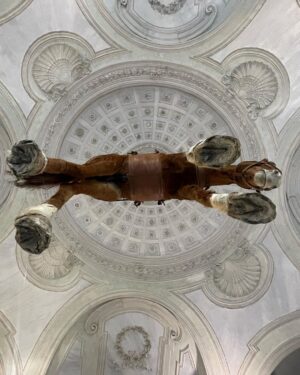 Daniela Collu Instagram - C’è un cavallo imbalsamato appeso in mezzo alla stanza di un museo: è un’opera di Maurizio Cattelan e si intitola Novecento. Ne ho visti un milione di cavalli nei musei, ritratti in posizione rampante, solenni nelle sculture equestri, dipinti nei paesaggi ottocenteschi, morenti nelle scene di guerra di tutte le epoche, a terra, galoppanti, in mandrie, solitari, ma così mai. 
Il collo è deformato, allungato dalla gravità e dalla tassidermia, le zampe a guardarle da sotto sembrano più tozze, più lunghe e larghe, e un senso di precarietà pervade i sensi, mentre si attraversa la stanza sotto questo peso galleggiante, immobile, inerme. Si chiama come il secolo in cui siamo nati, quello in cui la maggior parte delle sciagure che ora non sappiamo manovrare sono state costruite, un secolo di errori, di scoperte, di sconfitte e vittorie, di grandi passi per l’umanità e di crisi esistenziali senza ritorno. È la natura morta più disorientante, straniante e cruda che si possa immaginare, parla di simboli decaduti, di corpi infranti, di certezze mancate, di fallimenti annunciati. Di quel senso di impotenza e di inerzia umana che ancora, in un nuovo secolo, ci soffoca terribilmente. #unminutodarte