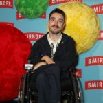 George Robinson Instagram - #ad I had a great time celebrating the launch of @smirnoffeurope WE DO US Live. While I love a good party, it’s way better when everyone can be a part of it. That’s why making nightlife more accessible is so important. @smirnoffeurope and Disability-led organization @tiltingthelens are working together to improve accessibility by supporting the Disabled community in clubs, bars and pubs - more to come! To everyone involved - thank you for such a fabulous night and showing easily it can be done. ************ Image Description: George Robinson is a white, masc wheelchair user. He has green eyes, cropped, dark hair, a moustache and dark stubble along his jawline. He is wearing a dark jacket and chinos and a white and black houndstooth polo shirt. He is wearing thick, textured brown socks and black leather shoes. On his lapel he has a small light green pin. He is positioned in front of a sky blue branding board, with the red and white Smirnoff logo repeated all over and red, green and yellow spheres covered in felt as a decoration. He is smiling for the picture and is at the Smirnoff ‘We Do Us Live’ event, celebrating accessibility in music. The event took place on 29/11 at 26 Leake Street in London.