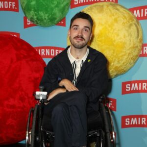 George Robinson Instagram - #ad I had a great time celebrating the launch of @smirnoffeurope WE DO US Live. While I love a good party, it’s way better when everyone can be a part of it. That’s why making nightlife more accessible is so important. @smirnoffeurope and Disability-led organization @tiltingthelens are working together to improve accessibility by supporting the Disabled community in clubs, bars and pubs - more to come! To everyone involved - thank you for such a fabulous night and showing easily it can be done.

************

Image Description: George Robinson is a white, masc wheelchair user. He has green eyes, cropped, dark hair, a moustache and dark stubble along his jawline. He is wearing a dark jacket and chinos and a white and black houndstooth polo shirt. He is wearing thick, textured brown socks and black leather shoes. On his lapel he has a small light green pin. He is positioned in front of a sky blue branding board, with the red and white Smirnoff logo repeated all over and red, green and yellow spheres covered in felt as a decoration. He is smiling for the picture and is at the Smirnoff ‘We Do Us Live’ event, celebrating accessibility in music. The event took place on 29/11 at 26 Leake Street in London.