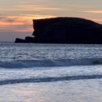 Louise Brealey Instagram - We drove west along the north coast of Scotland into the dazzle of a sunset and made it to the beach just before the sun slipped down behind a band of cloud. There was a smushed marigold on the tide line. I walked the quarter mile to our bit of the beach, where a scree of giant pebbles meet the sand. On my phone is a picture of mum sat here with a towel on her head. I put the marigold on the rocks. The Mexicans call it the flower of the dead and use its bright colours to guide the spirits of their lost ones to their shrines on the Dio de los Muertos. I ran my fingers through the fine white sand and let the sea and the sky do their thing.