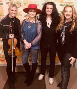 Pam Tillis Instagram - Behind the smiles….. words can’t even express how hard it is to watch all that’s happening on the world stage today. 
The gentlemen next to me is a fantastic guitarist and singer from Romania that happens to be playing with us… Alex Kilroy. His mom is a nurse at a hospital 200 miles from the Ukrainian border. All of my group.. Haley, Carson, Terry,
We know how fortunate we are to be playing music and trying soothe nerves and help people forgot for a moment how scary it all seems. So grateful. Even as we play my home state of Florida a world away our hearts are very much with the people of Ukraine who are suffering, those who are working for, fighting, and praying for peace. And also the brave Russians protesting and the other countries where people are taking to the streets with a message of love and not destruction. That’s all I got for now…….. this is just starting and I’m already emotionally spent.