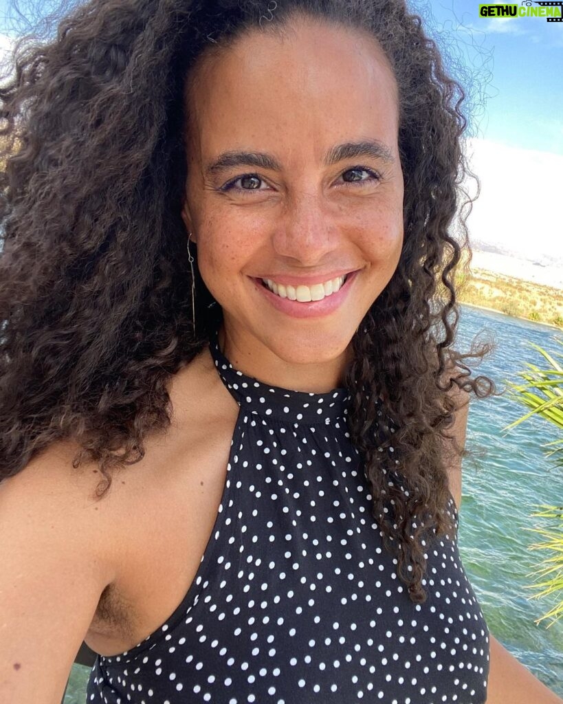 Parisa Fitz-Henley Instagram - Oh my goodness I’m so grateful! The last week and a half since my birthday (22 July) has been so rich. I spent the day itself driving through the desert on a solo cross country journey. This was my second birthday in a row in the desert, a place this water baby has come to appreciate so deeply. Following the example of friends who claim an entire month to celebrate their own births I decided to just stay open, navigating the habitual awkwardness I’ve had around celebrating mine at all. I decided to receive, to associate this time with an extra openness to joy and discovery — and what do you know, they showed up! 🤩 This is me in hot hot hot Nevada, in front of the ice-cold, beautiful Colorado river, with Arizona on the other side. I soooo recommend driving across a country — especially if you could use a reminder of the vastness of this planet, that in Truth we belong to all of it and that it belongs to all of us. I didn’t forget the lines that have been drawn, or the mindfulness required to navigate our many misunderstandings and shortcomings. I just got a chance to remember the bigger stuff more. What a blessing!!! Many thanks to all who sent messages last week. I wish I could have responded to them all individually. Please know how much they and you have been appreciated. I’m learning it’s always a good time to receive. It’s always the right time to feel joy. Nature is the definition of generosity and a reminder of our place in existence. There’s beauty even in dry expanses. Spirit is the ever-present, constant companion. It’s possible to not only step into the future with open arms, but also to gain new understandings of the past with an open heart. And of course, that magic abounds. Here’s to another year of life! Thank you for being a part of mine! Image description: A selfie of me smiling, curly brown hair out and blowing in the breeze, wearing a black halter top with white polka dots. Behind me, the green-blue Colorado River rippling, a bit of green foliage, white sand and a blue sky with whisky white clouds.