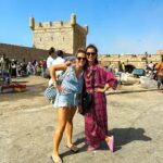 Vera Kolodzig Instagram – Dia 13:
Conhecida como a “Cidade Ventosa de África”, Essaouira atrai muitos kitesurfers durante o ano inteiro, no entanto há muito mais do que o areal a perder de vista, ou o cenário do Game of Thrones. O sultão Mohammed Ben Abdallah instalou-se aqui no século XVIII e contratou um arquitecto francês para desenhar uma cidade no meio do vento e da areia onde nada existia antes. Originalmente chamada de Mogador, o sultão mudou o nome para Essaouira que significa “bem desenhado”, com a sua mistura única de estilo marroquino e europeu.
Chegámos ontem à noite, já com mesa marcada num restaurante sugerido por um amigo, onde reencontrámos a amiga que fizemos em Tarifa na noite antes de iniciarmos a viagem. Acabámos num nightclub onde uma troca de olhares nos levou a conhecer os melhores guias que podíamos desejar.
A manhã de hoje foi na praia, com um mergulho salgado para lavar a alma. Surgiu então a possibilidade de ir à lota comprar o marisco mais fresco que alguma vez vi. Ao passar o arco do kasbah parecia todo um novo mundo, com as embarcações já atracadas e dezenas de pessoas a vender o que pescaram de manhã, enquanto as crianças se atiravam dos muros da fortaleza para o mar. Foi neste momento que decidi que se há locais para abrir excepções à minha habitual dieta, este é um deles, ainda assim mantendo os meus princípios – saúde e sustentabilidade. Duas lagostas, um caranguejo, camarões e uma conserva caseira, por 500dhr negociados pelos nossos amigos marroquinos. Depois levaram-nos pelo labirinto da medina até um terraço onde apenas famílias locais se deliciavam. Entregámos as nossas compras, e uma hora depois tínhamos uma mesa repleta das mais incríveis iguarias, por mais 60dhr – o custo do “aluguer” de um espacinho na grelha. 
Uma experiência que ficará para sempre nas nossas memórias e nos nossos corações, já com uma pequena nostalgia de uma despedida para breve.
Amanhã começamos a subir, de barriga cheia e inshallah sem caganeira!
.
.
.
#roadtrip #morocco #essaouira #localexperience #instatravel #seafood Essaouira – Mogador – الصويرة