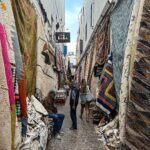 Vera Kolodzig Instagram – Dia 13:
Conhecida como a “Cidade Ventosa de África”, Essaouira atrai muitos kitesurfers durante o ano inteiro, no entanto há muito mais do que o areal a perder de vista, ou o cenário do Game of Thrones. O sultão Mohammed Ben Abdallah instalou-se aqui no século XVIII e contratou um arquitecto francês para desenhar uma cidade no meio do vento e da areia onde nada existia antes. Originalmente chamada de Mogador, o sultão mudou o nome para Essaouira que significa “bem desenhado”, com a sua mistura única de estilo marroquino e europeu.
Chegámos ontem à noite, já com mesa marcada num restaurante sugerido por um amigo, onde reencontrámos a amiga que fizemos em Tarifa na noite antes de iniciarmos a viagem. Acabámos num nightclub onde uma troca de olhares nos levou a conhecer os melhores guias que podíamos desejar.
A manhã de hoje foi na praia, com um mergulho salgado para lavar a alma. Surgiu então a possibilidade de ir à lota comprar o marisco mais fresco que alguma vez vi. Ao passar o arco do kasbah parecia todo um novo mundo, com as embarcações já atracadas e dezenas de pessoas a vender o que pescaram de manhã, enquanto as crianças se atiravam dos muros da fortaleza para o mar. Foi neste momento que decidi que se há locais para abrir excepções à minha habitual dieta, este é um deles, ainda assim mantendo os meus princípios – saúde e sustentabilidade. Duas lagostas, um caranguejo, camarões e uma conserva caseira, por 500dhr negociados pelos nossos amigos marroquinos. Depois levaram-nos pelo labirinto da medina até um terraço onde apenas famílias locais se deliciavam. Entregámos as nossas compras, e uma hora depois tínhamos uma mesa repleta das mais incríveis iguarias, por mais 60dhr – o custo do “aluguer” de um espacinho na grelha. 
Uma experiência que ficará para sempre nas nossas memórias e nos nossos corações, já com uma pequena nostalgia de uma despedida para breve.
Amanhã começamos a subir, de barriga cheia e inshallah sem caganeira!
.
.
.
#roadtrip #morocco #essaouira #localexperience #instatravel #seafood Essaouira – Mogador – الصويرة