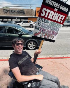 Zach Anner Instagram - As one of those writers and actors who works on several projects a year, but still can't make the minimum amount to get health insurance, this strike is pretty important to me! But it's not just about me obviously. It's about all the creative people who share their gifts and just want to make a living and be fairly compensated and appreciated for their work. #WGAStrong #sagaftra Image description: Zach, sitting in his wheelchair on a sidewalk in Burbank. he wears a shirt that reads 