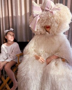 Sia Instagram - Waiting patiently ❣️ #GimmeLove - Team Sia [image description: a girl with a bow sitting next to Sia in a big white dress and white wig]