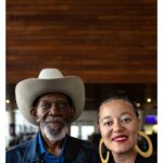 Stephen Hill Instagram - Deep Breath Breathe writer/director @jamieburtonoare of @jomajafilms with one of her many proud family members who showed up for our premiere screening. Uncle Paul Haire. Prior to our film block, I saw a beautiful film called Mosiah about Marcus Garvey. After that screening, I noticed Unc in his hat, in a sea of Garveyites proudly clad in Red Black and Green. I was able to meet him and share in the making of this photograph shortly after. Unc told me he inherited the hats of Grandaddy Eugene Henderson Burton, affectionately known as Doc. He said he switched his style up and started rocking the denim and cowboy boots to go with it. Now, he's purchased a few more cowboy hats to go with the collection. We chuckled when I told him he had on what they call a Canadian suit/tuxedo. It was great to have him there and see how proud he is of Jamie. Looking at this photo, I could talk all day about their beautiful brown faces anchoring and complimenting the mahogany wood backdrop or the balance between the weight of his hat and her earrings. But I find myself thinking of the etymology of the word Cowboy. It is said that black cow-HANDS were first derogatorily called cow-BOYS, and the name stuck. I'm also thinking I want to go riding. But most importantly, I'm thinking of how long after we stop breathing, even a single item endowed or imbued with our essence can connect, heal, and inspire those we leave behind for generations to come. We all live and breathe our allotment of that first breath. "The LORD God formed the man of dust from the ground and breathed into his nostrils the breath of life, and the man became a living creature” (Genesis 2:7) We breathe for those that no longer can. Aloha (Alo=face, Ha=breath) Now take a deep breath and give thanks to all that breathes life into you. ✊🏿❤️🙏🏿 #stephenhillphotos #leicaphoto #breathefilm #ericgarner #icanbreathe @detblackfilmfest #genesis27 John and Marlene Boll Family YMCA