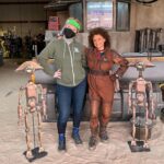 Bryce Dallas Howard Instagram - Let’s be real, we need more than a day – here’s how I’m celebrating #StarWars month and George Lucas’ birthday. #ThisIsTheMay⁣ ⁣ [ID 1: BDH, Peli Motto, and two pit droids take a break from building Mando’s ship to smile for a photo inside of Peli’s Hangar on Tatooine.] ⁣ ⁣ [ID 2-4: Posters for @thebookofbobafett Disney Gallery, @obiwankenobi, and Behind the Mac: @skywalkersound]