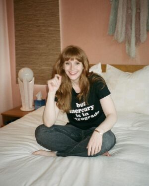 Bryce Dallas Howard Instagram - Mercury is Retrograde! In Virgo! To use the words of astrologer and writer @chaninicholas, “Good luck to us all!”⁣⁣
⁣
📸: Andie Jane (@andiejjane)⁣⁣
⁣⁣
[ID: BDH sits cross-legged on top of a fluffy white comforter. She points to her black t-shirt which reads, “but mercury is in retrograde.”]