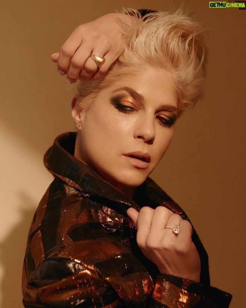 Selma Blair Instagram - Thank you @coveteur for highlighting my wellness journey 🤍 link in Stories Image 1: Selma has short blonde hair and is wearing a shiny black and bronze striped jacket. She has her hands lifted over head and face angled towards the camera, looking down. Her eye shadow is bronze and black. Image 2: Selma has short blonde hair and looks into a mirror as she holds a makeup tool for eyebrows from Guide Beauty Cosmetics. She wears a large emerald ring. Image 3: A headline from the Coveteur reads, “Selma Blair on Rediscovering Wellness Rituals That Work For Her.” Selma is quoted “now that I have cleared up some lost energy, I have the patience to witness my own imbalances.” Selma is shown sitting on a couch looking direct to camera.