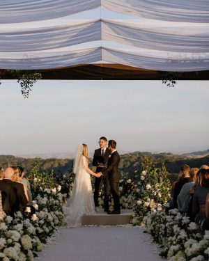 Taylor Lautner Instagram - CEREMONY
The ceremony was something we’ve been dreaming of for a long time. Along with the help of our wedding planners, we put in a lot of thought designing what exactly we wanted for this monumental moment and it came together even better than we had imagined. The ceremony location was at one of the highest points on the Epoch property which overlooks miles of wine country in Paso Robles. The colors surrounding us at this time of year are exactly why we love the Fall season so much. In an effort to provide shade and intimacy we installed a wooden truss system and semi sheer white draping, to create a relaxing and partially shaded ceremony location. White florals and lush greenery trailed up the columns of the wooden
structure and down the ceremony aisle. Beautiful white floral blooms surrounded us on a circle riser stage. As guests arrived by shuttle, they were invited to take a walk through the vineyard to the ceremony site. Our pastor and dear friend Judah Smith officiated the ceremony. It couldn’t have been more perfect. We exchanged hand written vows in front of the people we love most. Looking around and seeing the faces of each and every single person there, really put into perspective what is most important in life. Love. The sun set just as we said our “I Do’s” and the most beautiful pink sky was our backdrop as we walked back down the aisle as Mr. and Mrs. Taylor Lautner for the first time. 

Planning and Event Design @samkoma.world
Venue @epochwines
Photography @nicoleivanovphoto
Lighting @tn_event_designs
Floral Design @noonansdesigns 
Wedding Dress @winniecouture 
Grooms Tux @dolcegabbana