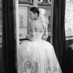 Vivienne Westwood Instagram - The Eline gown offers an unwavering sense of romanticism, embroidered with a Flora motif, taken from an archival couture lace. ⁠
⁠
The dress features a voluminous skirt with panniers, along with a straight neckline and transparent boned low hip corset bodice, accentuating the waistline. ⁠
⁠
The look is styled with fingerless gloves, echoing the decorative  detail of the dress. ⁠
⁠
Photography by @kingsley_ifill⁠
Styling by @florahuddart⁠
Talent: @elinehoyois⁠
⁠
#VWBridal #WestwoodBridal