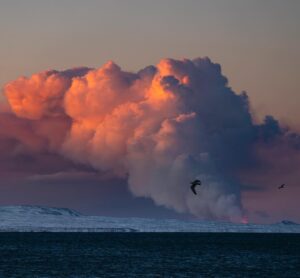 Chris Burkard Instagram - I jumped out of bed this morning for an early ski touring lap to catch sunrise... but much to my surprise I saw a warm glow radiating from the Reykjanes Peninsula and realized that a new volcano just erupted.  I texted my assistant @joelbarger_ from the top of the mountain -  who grabbed our long lens and nailed the shot just looking over the bay not far from our new studio. It’s moments like this in Iceland that continue to amaze me... a juxtaposition of normal life and sometimes devastating elements, locals continuing their day like any other Thursday but a beautiful fiery chaos erupts less than 45 minutes away.