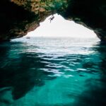 Chris Burkard Instagram – Mallorca, Spain. 2018 

Shallow enough to clearly see the sandy bottom.. but deep enough to make the fall safe. A magical element of the Balearic Islands – home to some of the most stunning deep water soloing & cliff jumping I’ve seen to date. This nameless cave route was never completed, Chris fell from the last hold. A couple hundred feet of monkey swinging from 3 dimensional roof holds made this particular line easily the longest deep water solo @chris_sharma attempted that day. By far – the best part was watching him fully excited to try this route like a kid nearly jumping off the boat…