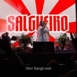 Maria Rita Instagram - hoje é dia de celebrar os 71 anos do nosso amado @salgueirooriginal! desde sua fundação, essa escola de samba desfila sempre com força, a paixão e a tradição… que venham muitos mais anos de glória, samba no pé e muitas histórias para contar! Vídeo: Guilherme Navarro/YouTube Samba da Maria no Vale do Anhangabaú - 18/03/2023 #PraTodosVerem Maria Rita em cima do palco com vestido branco e ao fundo um telão escrito “Salgueiro”.