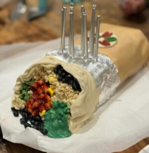Annabel Crabb Instagram - JUST LOOK at the burrito cake @glamgwenblake made at the request of her daughter. The corn is made from chopped up banana lollies. The silver foil is EDIBLE. The rice is rice bubbles tossed in melted white chocolate. A thing of delight. Happy birthday Honor. ❤️ ps this is Gwen’s photo, I took a bunch but none of them came out as nicely as Gwen’s for reasons that should be obvious haha. @chat10looks3