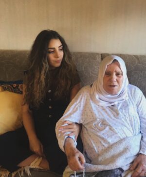 Gina Dirawi Instagram - Jag har alltid olivolja i mitt badrumsskåp.
Det är min farmor Fatimas fel.
När jag var liten brukade hon tvinga mig titta på medan hon oljade håret och flätade olivoljeflätor.
Oljan läker allt, sa hon.
Också det som gör ont.
De hade kvinnorna innan henne vittnat om.

Fatimas lägenhet i Sundsvall var ett heligt tempel tillägnat olivolja. 
Små fat, bräddfulla av flytande guld,prydde varje vrå, och medan hon följde världens händelser på TV:n såg jag olivoljeflätorna få liv. De vävde en historia om en ung tjej vars svett och arbete färgade olivlundarna. Om nätter tillbringade under olivträdens stjärnbelysta himlavalv.

I varje droppe såg Fatima ett kalejdoskop av minnen, ett helt universum osynligt för mina ögon, och som liten flicka grep jag desperat tag vid varje tillfälle att se henne måla liv i de delar som redan då fattades mig.

Häromdagen stod jag och oljade håret i över två timmar.
Det kanske låter överdrivet,
men sen hösten har tiden jag spenderat med oljorna ökat.
Minuter har förvandlats till timmar.
Jag smörjer och smörjer,
kroppen och håret.
Kammar och flätar,
och tänker på henne.

På allt hon fick säga och allt som tystades ner.
På hur hon fick sörja och hur hon förnekades sin sorg. 
På allt som togs ifrån henne och allt hon vann,
och hur jag ser konturerna av henne även i det här:

Att se klipp på youtube på sitt hemland
och längta,
titta på olivolja
och längta,
fläta sitt hår
och längta.

Jag är så jävla trött på att längta.

Trots det återvänder jag till oljan och flätorna.
I varje drag ger jag liv till en historia och ett arv som världen envist försöker tysta ner.
Det blir ett litet manifest, som bara jag kan se.
En tyst handling som sträcker sig flera tusen år tillbaka i tiden,
som tydligen ska läka de allra djupaste såren.

Ibland undrar jag om Fatima visste om att hon förberedde mig för de dagar då jag skulle behöva det som mest.
Ritualer som läker det onda,
det har jag farmor att tacka för🤍

📸: @daniel_stigefelt