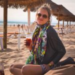 Ignacia Allamand Instagram - Había una vez un mundo, donde se podía viajar a lugares lejanos, y sentarse en la playa a tomar sangría viendo la puesta de sol sin mascarilla 🙃 Amo esta foto. El pelo chascón. El pañuelo de todos colores. La luz del crepúsculo y la cara de “Perdón por ser feliz con tan poco” 😂 que logró capturar una de mis mejores amigas de la vida. El vaso en la mano y la jarra que se asoma tímida por la esquina mostrando que gozar en grande nunca ha estado en discusión. El reloj swatch que ya en ese entonces estaba pasado de moda y el bolsito gris lleno de bolsillos y cierres, imprescindible para guardar mapas y guías turísticas y cuadernos y cámaras y puchos y encendedores. Ahora todo eso se condensa en un solo aparato y por suerte ya no fumo. ¿Que nostalgia o no? No solamente de viajar, si no de viajar como antes. Sin WhatsApp, sin interrupciones, sin la necesidad de etiquetar ni de agregar la ubicación a nada. Entiendo la contradicción de hablar de esto precisamente en una red social, pero a veces me agarra el fantasma de los recuerdos y me remueve la guata y no me aguanto de compartir lo lindo que era la no necesidad de compartir 🤪 Sobretodo los jueves, que gracias al #throwbackthursday tengo la excusa perfecta para contagiar mi saudade y mis recuerdos. Esto fue en Portugal. El año 2011. Tenía 29 años y quería comerme el mundo entero. O tomármelo para ser sincera. Durante esta pandemia he vuelto a mirar las fotos de ese viaje una y otra vez, compulsivamente, obsesivamente, como si verlas fuera una forma de viajar no solo a otros lugares, si no que también en el tiempo. Y a ratos eso me ha hecho muy, pero muy feliz. Otras me ha dado pena. Pero de esa linda, que más que tristeza, es emoción. ¿Les gusta mirar fotos de otros tiempos? ¿Será que todo tiempo pasado fue mejor? Abrazo a todos. Tomen agüita. Ánimo a los que lo están pasando mal. Besitos a los que tiran mala onda. Y besotes a los que mandan buena vibra. #queendelmuchotexto