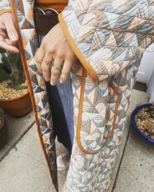 Jasika Nicole Instagram - I didn’t hop onto the quilted jacket trend til @byhandlondon released the #NerrisaCoat pattern a couple months ago. I loved the collar, the oversized fit and the long length, three elements that I had not previously seen in quilted coat patterns, and I had the *perfect* fabric for it- a geometric reversible quilted cotton smack in the middle of my color palette from @corefabrics. The pattern is very simple, pretty beginner friendly, and requires very little fit adjusting because it’s so oversized. I made the smallest size available (it goes up to a size E/ 61.75” bust) but it’s still incredibly roomy, like I could probably fit a sweater AND another coat under this lol. If I were to make it again I would probably slim down the fit by a couple inches and shorten it to shin length, which I might still do, but I wanted to get some wear out of this length before I chopped it up. I opted not to add buttons to the front and just have this be a kind of open jacket for layering. I made the bias binding myself and this is the only issue I had with the pattern- it says you need 5 meters of binding but I easily used 3 times that much for this view (I stopped counting after the third time I had to pull out my tools to make more tape 😵‍💫), so maybe that amount was meant for the shorter version of the jacket (because it doesn’t give different amounts for the different views). Thankfully I had just enough tencel scrap fabric to make all the tape I needed. The bias binding gives the jacket a nice pop of color while still feeling a bit neutral and I love how the colors in the fabric and tape play off of each other. I’m on the fence about the patch pockets on my version and think it would look even better with inset pockets, and because of the bulk of the quilted fabric, the drop sleeves look a little funky at the seams(I prefer inset sleeves). But those design choices are what makes this such a simple and quick pattern to finish, and I’m still happy with how this came out. The fabric is structured but soft and wearing it feels like you’re draped in a blanket cocoon- it actually makes a pretty great housecoat if you’re careful to not trip over it 😂