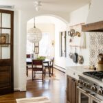 Lauren Liess Instagram - Another peek into that kitchen where you can spy the breakfast room through the archway. An antique family table became the centerpiece for the breakfast room which we decorated simply with antique Spanish colonial chairs and a hide rug for easy cleaning. A double pot rack over the old radiator is within reach of the new range. {tile is “sol di folium” from my collection with @architessa | cabinetry is the “bohemian” from my collection with @uniquekitchensandbaths and vintage runner accessories are from @laurenliessandco | renovation by @carrmichaelconstruction | design by us at Lauren Liess Interiors | photo by @helennorman for my book #feelslikehome where I share all the “whys” behind the design of the entire house }