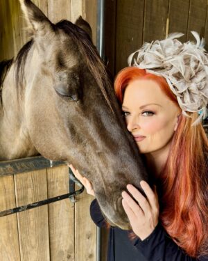 Wynonna Judd Instagram - My favorite horse won’t be @churchilldowns this weekend, but we’re still celebrating in style together! 🤍🐎 (I’m so excited that I’ve been wearing my Derby fascinator around the farm) 😆 Tune in to NBC THIS SATURDAY to see me perform the national anthem at #KentuckyDerby150!! Comment below who you’re cheering for…👇🏼 #WYinKY #KyDerby #KD150 #ChurchillDowns #NationalAnthem