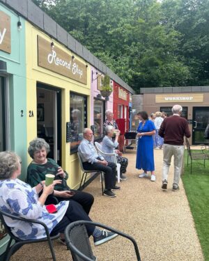 Anneka Rice Instagram - Oh my goodness. I went to Birkenhead, near Liverpool, today, to visit our Dementia Village, built on Challenge Anneka in 2022. It is flourishing. On a piece of wasteland a team of epic volunteers, builders, craftsmen, built an entire memory village - with pub, post office, record shop, cafe, bakers, cinema, bowling lawn, landscaped gardens! We worked in the pouring rain, in a recession, it was beyond stressful - but I thought my heart would burst, visiting it in the sunshine today, seeing what a difference it has made in this Wirral community. They now have over 400 volunteers helping out. The idea is that someone with dementia can wander safely round the village, dropping in on shops, listening to their favourite record, watching a film, having a singalong in the pub, doing whatever they want. It’s liberating for them and their loved ones because on every corner, sitting in the shops, offering them a cuppa in the cafe, there are carers to help them, chat to them, play bowls with them, sing with them. Each shop is curated to trigger memories. I went down a rabbit hole of memories seeing the Green Shield Stamps in the Post Office! IT IS BRILLIANT. I would love to see this rolled out across the UK. Well done @ageuk_wirral for having such vision 🩵🩵🩵 @age_uk #dementia @alzheimersresearchuk #village #ChallengeAnneka #charity #volunteers #community #joy @channel5_tv