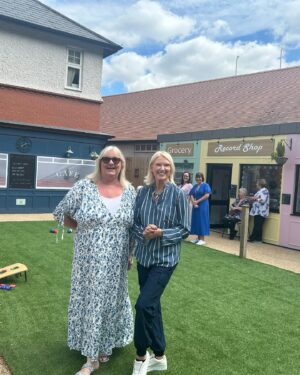 Anneka Rice Instagram - Oh my goodness. I went to Birkenhead, near Liverpool, today, to visit our Dementia Village, built on Challenge Anneka in 2022. It is flourishing. On a piece of wasteland a team of epic volunteers, builders, craftsmen, built an entire memory village - with pub, post office, record shop, cafe, bakers, cinema, bowling lawn, landscaped gardens! We worked in the pouring rain, in a recession, it was beyond stressful - but I thought my heart would burst, visiting it in the sunshine today, seeing what a difference it has made in this Wirral community. They now have over 400 volunteers helping out. The idea is that someone with dementia can wander safely round the village, dropping in on shops, listening to their favourite record, watching a film, having a singalong in the pub, doing whatever they want. It’s liberating for them and their loved ones because on every corner, sitting in the shops, offering them a cuppa in the cafe, there are carers to help them, chat to them, play bowls with them, sing with them. Each shop is curated to trigger memories. I went down a rabbit hole of memories seeing the Green Shield Stamps in the Post Office! IT IS BRILLIANT. I would love to see this rolled out across the UK. Well done @ageuk_wirral for having such vision 🩵🩵🩵 @age_uk #dementia @alzheimersresearchuk #village #ChallengeAnneka #charity #volunteers #community #joy @channel5_tv