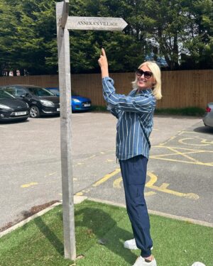 Anneka Rice Instagram - Oh my goodness. I went to Birkenhead, near Liverpool, today, to visit our Dementia Village, built on Challenge Anneka in 2022. It is flourishing. On a piece of wasteland a team of epic volunteers, builders, craftsmen, built an entire memory village - with pub, post office, record shop, cafe, bakers, cinema, bowling lawn, landscaped gardens! We worked in the pouring rain, in a recession, it was beyond stressful - but I thought my heart would burst, visiting it in the sunshine today, seeing what a difference it has made in this Wirral community. They now have over 400 volunteers helping out. The idea is that someone with dementia can wander safely round the village, dropping in on shops, listening to their favourite record, watching a film, having a singalong in the pub, doing whatever they want. It’s liberating for them and their loved ones because on every corner, sitting in the shops, offering them a cuppa in the cafe, there are carers to help them, chat to them, play bowls with them, sing with them. Each shop is curated to trigger memories. I went down a rabbit hole of memories seeing the Green Shield Stamps in the Post Office! IT IS BRILLIANT. I would love to see this rolled out across the UK. Well done @ageuk_wirral for having such vision 🩵🩵🩵 @age_uk #dementia @alzheimersresearchuk #village #ChallengeAnneka #charity #volunteers #community #joy @channel5_tv