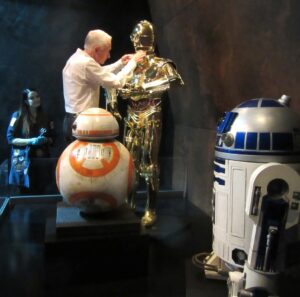 Anthony Daniels Instagram - I’m hugely appreciative of all your kind words about my book. I do try to read all your comments but can’t possibly respond to everyone who asks, otherwise Instagram would become a job instead of a joy. 
Today I was buying a coffee at Victoria Station in London and a complete stranger approached me to tell me how much he was enjoying reading the book. Magic!
This pic illustrates a story I tell on pages 195-196. I’m adjusting Threepio’s position in the Star Wars and The Power of Costume exhibition in Times Square NYC. Joanee Honour, from the archive team at Lucas Film, looks on anxiously.
@lucasfilm #thepowerofcostume #bb8 #r2d2 #c3po #iamc3po #victoriastation @dkbooks @starwars