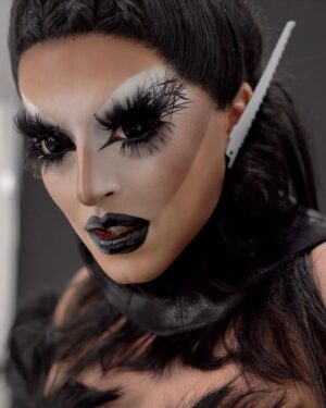 Cherry Valentine Instagram - One of my favourite looks from the “Iconic” video. This look focuses on restriction, Fetish, and fashion. Inspired by the work of Thierry Mugler’s S/S 1997 couture collection, specifically the leather carapace. Since I discovered this collection I’ve been absolutely in awe of the creativity and craftsmanship, & working with @freakcouturemcr on some adaptations, we brought it to the world of drag!

This look is made up of a full leather stitched carapace, with neck collar, leather gauntlets and floor length draped mesh underskirt. The trim is made from wefts of hair, and I couldn’t be more in love. This hair is by @josephmannhair and I chose it because I wanted that high pulled back snatched fantasy. I put saw blades on the ears to give it that little extra bit of danger, along with the standard black out @scleracontacts with my go-to nails 🤤

ICONIC is out now on streaming platforms. Link in bio for the Official Music Video.