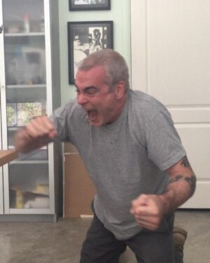Henry Rollins Instagram - In case you ever wondered what Henry looks like after doing push-ups on his knuckles. 👊😡👊😡

#henryrollins #graytshirt #screamingtomatoface #officeinsanity #henryandheidi