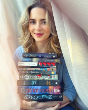 Holly Deveaux Instagram - I’m just a girl, sitting in a curtain, holding some of her precious books, wondering what else everyone else is reading. 

This is my bat signal in the sky to all readers reading - who knows some great female-led Sci-fi or fantasy? Particularly anything featuring neuro-divergent characters!! 

#fantasy #sciencefiction #seaoftranquility #stormlightarchive #nameofthewind #tosleepinaseaofstars #books #thebearandthenightingale 

📸@jesserath - thanks I know this was a weird one