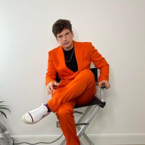 Jacob Dudman Instagram - Splash of colour 🍊 
For @fatenetflix press.

Styling: @ellalouisegaskell 
Make-up: @tonihowardmakeup 

Suit: @stellamccartney 
Chain: @tillysveaas 
T-shirt: @basicrights 
Shoes: @malonesouliers