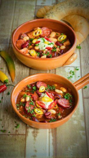 Josef Nemrava Instagram - Fazolová polévka s uzeným masem a klobásou

Mám doma samé holky, tak si chilli přidávám, až na talíři, ale pokud nemáte s pálivým problém, tak klidně přidejte v průběhu vaření.

1 kg uzeného masa (do polévky půjde jen kousek, zbytek je k bramborové kaši, na šunkofleky, nebo třeba do knedlíků)
1 měkká papriková klobása (já měl Šumavskou)
1 ČL sádla
1 cibule
1 plechovka červených fazolí
1 plechovka bílých fazolí
6 stroužků česneku 
3 bobkové listy
8 kuliček nového koření
10 kuliček pepře
1 PL mleté papriky
120 g rajčatového protlaku
Hrstičku sušené majoránky
Sůl
Pepř

Na dochucení:
Zakysanou smetanu a čerstvé chilli 

Nejprve si uvaříme uzený vývar tak, že do hrnce dáme uzené maso, zalijeme studenou vodou, přidáme cibuli, 3 stroužky česneku, nové koření, bobkový list, celý pepř, lžičku soli, přiklopíme a vaříme maso do měkka, zhruba 90 min.
Když máme vývar hotový, tak si v hrnci rozpálíme sádlo a na něm zarestujeme klobásu nakrájenou na kolečka.
Klobásu pak vyndáme a na výpeku zarestujeme cibuli do sklovata.
Následně zarestujeme mletou papriku a pak protlak.
Přidáme 1 l uzeného vývaru (zbytek si můžeme zamrazit a použít příště), nadrcený česnek, opepříme, přiklopíme a 15 minut provaříme.
Po 15 minutách přidáme fazole i s nálevem, případně dosolíme a ještě 10 minut provaříme.
Nakonec přidáme kolečka orestované klobásy, uzené maso na kostičky a rozemnutou majoránku.
Na talíři už si přidá každý sám zakysku a čerstvé chilli dle chuti.

Dobrou chuť