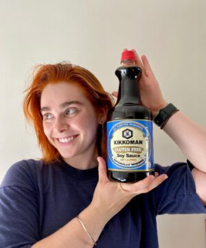 Maiah Stewardson Instagram - i FOUND IT !!¡¡!! months of searching for this XXL gluten free kikkoman soy sauce. praise be. long live my hidden local asian grocer ❤️‍🔥look at her in all her glory. yom. 

[ID: Maiah holds a large bottle of soy sauce up next to their face. the bottle has a blue and white label with red lid. Maiah’s expression is open and happy, and their eyes look to the side]