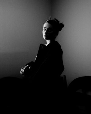 Maiah Stewardson Instagram - w love 🧚🏼‍♂️🌶☁️

[ID image 1: a black and white portrait of Maiah’s side profile. They have their hair in two space buns and delicate flowers lining their jawline and hair. 
Image 2: a portrait of Maiah wearing an all black coat with fluffy black slippers. They are standing with their feet close together and hands clasped 
Image 3: Maiah looks back at the camera. Their hands are lightly clasped and shadows hit the side of their body and face].