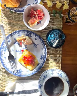 Maria Dias Instagram - O pequeno-almoço em Marrocos é divinal, qualquer que seja o deus ou allah que adore. É sempre vegetariano, vegan só mesmo o pão do post anterior, e as deliciosas compotas de figo, alperce e amlou sem mel.
Estas panquecas folhadas das fotos chamam-se msemen, são feitas frescas na chapa todas as manhãs e, tal como parecem, são uma maravilha. Podem-se comer doces ou salgadas e fazem-se com uma série de dobras e viragens para ficarem que nem uma massa folhada leve. São irresistíveis com Amlou. Ou Amlou não fosse das coisas mais irresistíveis para comer em Marrocos, não deixem de provar. É manteiga de amêndoa com óleo de argão, algumas levam mel também.
Bahgri são as panquecas alveoladas, das mais leves que já provei. Parece que estamos a comer uma renda sedosa. Fica deliciosa com fruta fresca (romã na estação) ou/e compota.
Café (tipo café turco, bem forte e bem bom), chá de menta fresquinho e sumo de laranja ou de romã também estão sempre no menu.
Comem-se muitos ovos, em omeletes finas a que juntam cebolinho e aromáticas ou cubinhos de pimento.
Azeitonas pretas curadas, bem diferentes das nossas, mais salgadas e aromáticas servem de contraponto entre os doces. 
Um pequeno-almoço num jardim, numa das ruas confusas ou num Riad valem mesmo a pena. São lentos, frescos e bem bons.