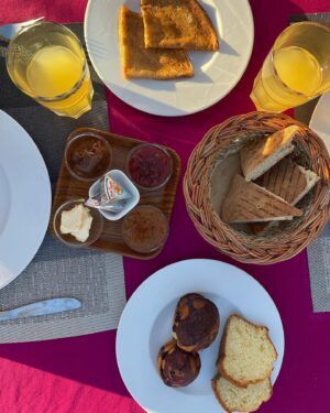 Maria Dias Instagram - O pequeno-almoço em Marrocos é divinal, qualquer que seja o deus ou allah que adore. É sempre vegetariano, vegan só mesmo o pão do post anterior, e as deliciosas compotas de figo, alperce e amlou sem mel.
Estas panquecas folhadas das fotos chamam-se msemen, são feitas frescas na chapa todas as manhãs e, tal como parecem, são uma maravilha. Podem-se comer doces ou salgadas e fazem-se com uma série de dobras e viragens para ficarem que nem uma massa folhada leve. São irresistíveis com Amlou. Ou Amlou não fosse das coisas mais irresistíveis para comer em Marrocos, não deixem de provar. É manteiga de amêndoa com óleo de argão, algumas levam mel também.
Bahgri são as panquecas alveoladas, das mais leves que já provei. Parece que estamos a comer uma renda sedosa. Fica deliciosa com fruta fresca (romã na estação) ou/e compota.
Café (tipo café turco, bem forte e bem bom), chá de menta fresquinho e sumo de laranja ou de romã também estão sempre no menu.
Comem-se muitos ovos, em omeletes finas a que juntam cebolinho e aromáticas ou cubinhos de pimento.
Azeitonas pretas curadas, bem diferentes das nossas, mais salgadas e aromáticas servem de contraponto entre os doces. 
Um pequeno-almoço num jardim, numa das ruas confusas ou num Riad valem mesmo a pena. São lentos, frescos e bem bons.