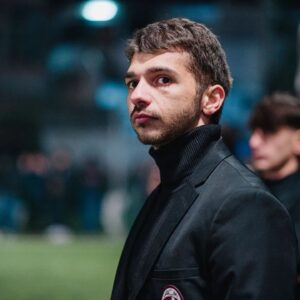 Mirko Mastrocinque Instagram - Qui alla YTL esistono le figure degli allenatori per delle squadre che, fondamentalmente, non si allenano. D'altronde è una competizione di content creators che, di base, tifano o vestono le maglie di squadre reali di calcio, per portarle alla vittoria rappresentandole al meglio nella loro storicità.
E questa idea la si porta in campo, o per lo meno è quel che faccio io.
Allora i barlumi del creator  mi dicono che devo andare ad interpretare quel ruolo, che devo immedesimarmi in esso per farlo bene. Così ho passato più di qualche ora a vedere i video degli avversari, a studiare l'impatto dei cambi in rosa, a tessere i fili comunicativi di un gruppo che si vede solo alle partite. Ho passato tempo a ragionare coi se e coi ma e sono anche sceso a patti con la fortuna nell'indovinare cambi e scelte che, a posteriori, sono sempre risultate così dannatamente giuste o sbagliate.
Alle volte son stato anche pagliaccio perché l'allenatore è un parafulmine, è un alibi, è quello che dà una interpretazione alle partite o estremizza la comunicazione con risultati spesso grotteschi.
È un gioco quello della YTL dove non si vince nulla di importante. Non ti cambia la vita se vinci o se perdi e non la cambia a chi ti vede.
Eppure mi diverte e, come diceva Saba, ho deciso che "Della festa anche io son parte".