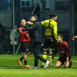 Mirko Mastrocinque Instagram - Qui alla YTL esistono le figure degli allenatori per delle squadre che, fondamentalmente, non si allenano. D'altronde è una competizione di content creators che, di base, tifano o vestono le maglie di squadre reali di calcio, per portarle alla vittoria rappresentandole al meglio nella loro storicità.
E questa idea la si porta in campo, o per lo meno è quel che faccio io.
Allora i barlumi del creator  mi dicono che devo andare ad interpretare quel ruolo, che devo immedesimarmi in esso per farlo bene. Così ho passato più di qualche ora a vedere i video degli avversari, a studiare l'impatto dei cambi in rosa, a tessere i fili comunicativi di un gruppo che si vede solo alle partite. Ho passato tempo a ragionare coi se e coi ma e sono anche sceso a patti con la fortuna nell'indovinare cambi e scelte che, a posteriori, sono sempre risultate così dannatamente giuste o sbagliate.
Alle volte son stato anche pagliaccio perché l'allenatore è un parafulmine, è un alibi, è quello che dà una interpretazione alle partite o estremizza la comunicazione con risultati spesso grotteschi.
È un gioco quello della YTL dove non si vince nulla di importante. Non ti cambia la vita se vinci o se perdi e non la cambia a chi ti vede.
Eppure mi diverte e, come diceva Saba, ho deciso che "Della festa anche io son parte".