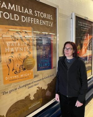 Natalie Haynes Instagram - It is such a thrill to see these posters out in the wild! Thank you to @picadorbooks for this amazing campaign 🧡🧡 Please note lack of glasses because on my way back from the gym. Bonus fact: I asked a stranger to take this pic in the 1 minute before her train arrived, and she said yes