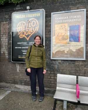 Natalie Haynes Instagram - It is such a thrill to see these posters out in the wild! Thank you to @picadorbooks for this amazing campaign 🧡🧡 Please note lack of glasses because on my way back from the gym. Bonus fact: I asked a stranger to take this pic in the 1 minute before her train arrived, and she said yes