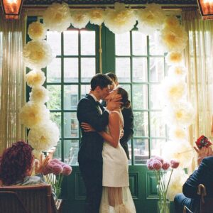 Barton Cowperthwaite Instagram - We were married in the Solarium next to the Piano Bar at the Hotel Chelsea. Choosing the Chelsea was an easy decision. It’s iconic, filled with art and history. I grew up on 22nd between 5th and 6th, and remember it in its late 90’s crumbling glory. The Solarium, small and perfect for our 35 guests, has a beautiful skylight running the length of the room. Decorated with plants and greenery, it was perfect as it was, requiring minimal decoration.

Our best friend Sammy (Bart’s best friend since birth) who knows us as individuals and as a couple better than anyone else, officiated the ceremony. It felt comfortable, relaxed, and unfussy. Our violinist played as we each walked down the aisle with our parents. The three of us stood in front of an arch I constructed from wooden dowels, tissue paper flowers from Etsy, Velcro, and hot glue. We were flanked by two bunches of my favorite Allium flowers. We each took a long moment to take in the space before our vows. We wanted to be as present as possible. 

After the ceremony, we had a champagne toast, and Bart’s brothers each said a few words. Our guests stayed for a cocktail hour while we left to do photos in our room. We left the Hotel Chelsea and went to the West Village with our photographers. Standing on a corner next to a tipped-over trash can for 15 minutes, trying to hail a cab, we were met with honks and cheers. It was a quintessential New York moment, a reminder that the city stops for no one.

We walked around the West Village, taking photos at all our favorite neighborhood spots. We stopped by Grove Apothecary to see our pharmacists, who have always taken such good care of us. We visited the Jane laundromat, where Bart has made friends with everyone who works there. We were all heartbroken when he got sick, but no one was as crushed as our friends at the laundromat. We dropped in at Casa Magazines, where Bart buys copies of the magazines he’s published in. This community is a part of our everyday lives. They’ve made our New York City feel like a close knit small town. Their kindness and care got us to the other side of a terrifying time, and we wanted to share a piece of the other side with them.