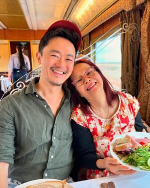 Benjamin Law Instagram - Ticking off an all-time bucket list item for Mum’s 70th birthday … BY TAKING HER ON THE FRICKIN’ GHAN. 
 Feeling damn lucky to travel close to 3000km through the heart of the continent on such an iconic railway, starting in Adelaide on Kaurna Country, then chasing sunrise at Marla on Anangu Pitjantjatjara Yankunytjatjara Land, having stunning off-train nature experiences at Mparntwe (Alice Springs) and Katherine on Jawoyn Country, before finally pulling into Darwin on lush Larrakia Country. 

It’s wild. You honestly can’t quite comprehend the scale of Australia until you experience it like this. 

But what was really staggering for this daughter of a restaurateur (Mum) and son of a restaurateur (me) was the all-inclusive* wine list and menu of fine-dining quality local fare (think: crocodile dumplings, local barramundi, buffalo massaman curry, mango parfait) they served up every day. We’re still processing how these peeps make food this good on a moving vehicle. 

Shout out to the entire Ghan crew who gave us the Gold Service (literally) treatment, especially Yohan, Rami, Darlene, Ralph and Imogen for taking extra special care of Mum. 

And massive thanks to the utter legends at @journeybeyondrail for making a lifelong dream of Mum’s come true. 

If you’re considering one of their iconic trips between Adelaide and Darwin (The Ghan), Sydney and Perth (Indian Pacific), Brisbane and Adelaide (Great Southern) or Adelaide and Melbourne (The Overland), follow them on Insta for inspiration and travel porn. 

Can’t recommend it enough. 

Oh, and happy birthday to the Ghan too. Lookin’ good for a gal who’s just turned 95.

*N.B. “All-inclusive” is now my safe word. 

#journeybeyondrail #theghan #australiabytrain #gifted