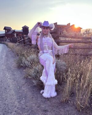 Ilona Verley Instagram - “You were a mirage, you’re not really there”
🐎🐎🐎🐎
Inspired by @slayyyter & the cowboys music video!
🐎🐎🐎🐎
This look was originally made for me a few years ago by @connormccalden who did up the chaps/ bra & gloves for me when I was in Toronto for a few months and running out of outfits at the time!
I later made the hat and the bodysuit to go with it & @hauszuk helped me stone everything! 
🐎🐎🐎🐎
I’m so happy to have finally gotten to shoot this look & to do it with my incredible mom @sandiverley who took off a whole weekend to drive us up home to the canyon and literally camp until it was cool enough for us to drive to the ghost town to actually shoot… our one day trip turned into a 3 day adventure!
THANK YOU MOM!
🐎🐎🐎🐎
Hair was done for me the MORNING of by @the.girlfriendexperience
Also a big shout out to sheisbliss for helping me stone and get myself together that morning as well!
Hat was originally from @rockin_cowboy_clothing_company painted and transformed by me! (Reel coming soon on the DIY) 
Boots were from @onlymaker_shoes transformed by sheisbliss & myself! 
Earrings by @sadndn_ 
🐎🐎🐎🐎
I used to try to be so independent and do everything myself, but the last little bit, I’ve been giving up the perfection complex of wanting to do it all alone & it has helped me see that creating is not only easier but much more rewarding when you work with others, especially the people you LOVE!
The funny thing is to me the most perfect art has been the stuff I’ve done with friends… not the stuff I’ve done alone… (learning lesson for those struggling with giving up control / dealing with the typical artist perfection complex) 
🐎🐎🐎🐎
#cowgirl #cowgirlfashion #cowboyhat #purple #lavenderhair #humanhairwig #drag #dragqueen #purplemakeup #onlymaker #festivalfashion #ravegirl #ravegirls
