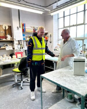 Joe Lycett Instagram - Back in October last year I went along to @duchesschina1888 in Stoke-on-Trent to see how they were getting on with the Slags Vase. It’s a very special sprawling place, steeped in history and so much love for ceramics and their production. I was fortune to meet Gordon who is their master modeller, whose job it was to measure up my original piece-of-shit design and recreate it in bone china. I’d like to apologise to Gordon for making him stoop so low as to recreate my vase. I also got to see their production line and some of the other work they do for the royals, amongst others, and make a mug, which I’m pretty sure I watched someone immediately put into a bin. 

It was a total delight working with Gordon, Jason and the team on this project, all beautifully coordinated by @theymadethistagram 

The limited edition vases (only 250 made) go on sale to my mailing list tomorrow morning and all the money I make from the sales will go to @artsemergency. Sign up at joelycett.com