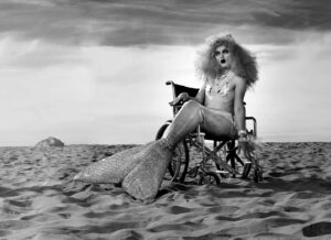 Magnus Hastings Instagram - So many super gay references in this shot. Another Why Drag?  out take .. I had to carry @xoxoscarlettletters across the beach as she was all wrapped up in her @mr.davidglamamore original tail .. an example of how San Francisco showed up for me .. the wheelchair belonged to the late great #phatimarude ❤️❤️#magnushastings #whydrag #glamamore #sanfrancisco