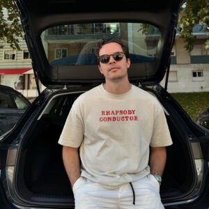 Martim Sousa Tavares Instagram - Rhapsody conductor ✌🏻

Vi esta t-shirt e achei que era, em duas palavras, um bom resumo deste mês de julho:
Rhapsody, porque tive um pouco de tudo, inclusive a "Rhapsody in Blue". 
Conductor porque é a palavra inglesa para maestro. Dirigir concertos foi intenso e muito fixe. No Brasil, dirigir é conduzir. Também fiz muito disso este mês (quase 6000kms 😮‍💨) e boa parte deles foi com o rabo sentado neste Seat Leon 🦁 que a @seatportugal achou por bem emprestar-me. Não podia ter vindo mais a propósito e fomos muito felizes juntos! 🥲