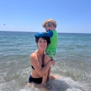 Rosanne Mulholland Instagram - Ah, a maternidade e as férias....
Bisous.
💛

#PraTodosVerem Uma sequência de três fotos na praia. Na primeira, o Davi, menino branco  de 3 anos com roupa de praia verde, está em pé cima das pernas da mãe, Rosanne, mulher branca de biquíni azul marinho, que está sentada na parte rasa da praia, onde a água cobre as pernas. Davi está se pendurando em sua cabeça enquanto ela mantém um sorriso meio desesperado. A segunda é uma variação da primeira. O sorriso não mostra os dentes e é mais debochado. Uma onda bate nas costas de Rosanne. Na terceira foto,  a água recuou e vemos as pedrinhas da praia. Davi está pendurado de forma que seu rosto está escondido atrás da cabeça da mãe. Rosanne agora dá um sorriso sincero. Fim da descrição.