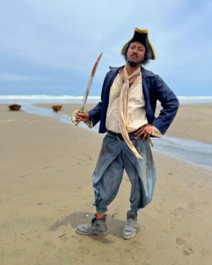 Samba Schutte Instagram - Today’s (Our) Flag (Means Death) Day, and many of you have asked for deets on my character Roach in Season 2🪳 Here you are🏴‍☠️ 
Details on the costumes during fittings and after weathering and aging. It was great collaborating with Costume Designer Gypsy and being able to implement my own backstory. For the Red Flag fit I wanted him to have a headband because a chef never gets hairs on his meals. Unless it’s on the menu, or you’re serving the British👨🏾‍🍳
For his new fit, Roach got to have more jewelry this season because he became a better pirate. I chose 3 rings. The Lion to symbolize the Atlas Mountains where he hails from. The 2 headed Snake, because you have to always watch your back as a pirate. And a Celtic looking ring, because Roach has a tender spot. Like with his mother’s scarf. And of course his talisman necklace that he always wears, with every costume🪬At first it was gonna be a long sleeve shirt, but Jenkins wanted me to show off my sexy dessert making arms. Rightly so…..💪🏾
On his belt he had meat hooks, his cleaver as a weapon and of course, a wooden spoon for self defense🥄
I’ve never worn Doc Martens before and let me tell you, I don’t know how people smaller than me do it, those things weigh a ton each! Now imagine running on the beach in them👀
More deets in stories but I loved every minute of dressing up as and playing this chaotic dude🫶 
#ourfladmeansdeath #ofmd #ofmdseason2 #roach #cosplay #bts